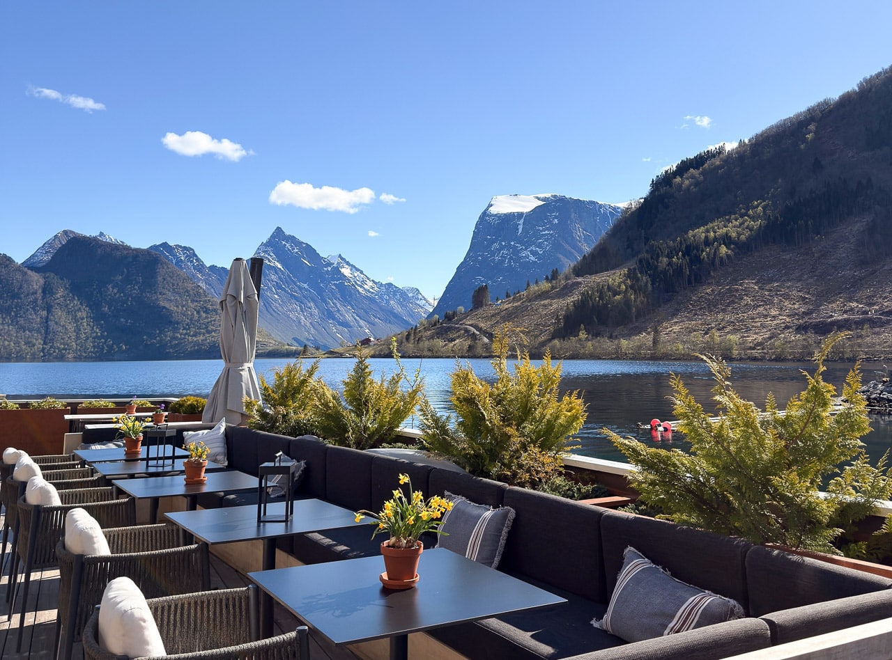Uteservering med utsikt over fjord og fjell i sollys